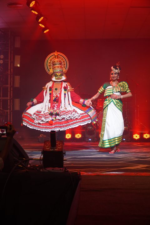 Kathakali performer and a Bharatanatyam dancer holding hands on stage under red lights