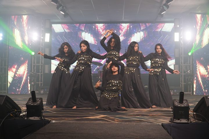 Dance troupe in black coin-embellished costumes striking a pose on stage